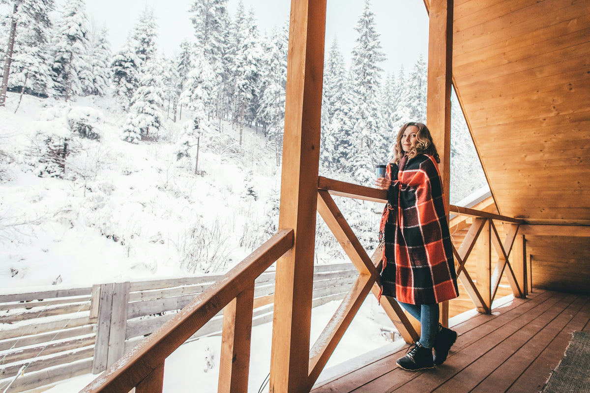 Woman wrapped in a red plaid blanket on a snowy cabin porch
