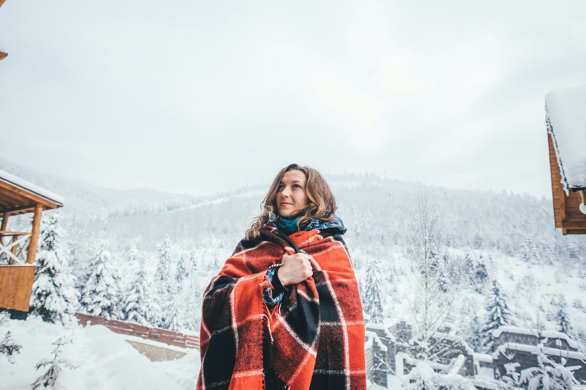Woman wrapped in a plaid wool blanket in a snowy forest